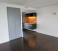 Empty room with wooden floor, white walls, gray cabinet, black shelves, and an open door