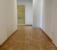 empty hallway with wooden parquet flooring, white walls, ceiling light, and a closed door to a bathroom