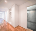 corridor with wooden floor, white walls, ceiling lights, large wardrobe, glass door to bathroom
