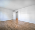 Empty room with wooden floor, white walls, two doors, windows