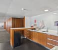 modern kitchen with wooden cabinets, white countertops, stainless steel sink, faucet, trash bin, coffee machine, and a bowl on the counter