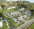 Group of houses on a hillside, all with green roofs, solar panels, balconies, gardens, driveways