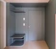 Minimalist entryway with gray walls, integrated shelving, and metal door with silver handle and lock. A hanging rod and a bench-like shelf are attached to the wall.