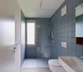 Blue tiled bathroom with shower, toilet, sink, and glass door