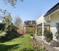 House with solar panels, garden with lawn, plants, and trees, pathway, swing, and a wooden deck.