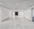 Long, wide hallway with white walls, a tiled floor, and a suspended ceiling with recessed lighting. The hallway appears to be in a commercial or office building, with doors leading to other rooms or offices on either side.