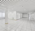 Large open commercial space with white walls, tiled flooring, and a suspended ceiling with recessed lighting. The space appears to be empty and ready for use.