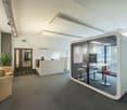 Contemporary design, white furniture, gray carpet, glass-enclosed cubicle, two stools, desk, modern lighting fixtures, potted plant, exit sign, two chairs