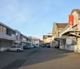The image shows a commercial area with several buildings, including a large building with a red 'C' sign on it. There are parked cars in the paved parking lot in the foreground, and the buildings have a mix of modern and older architectural styles.