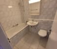 bathroom with sink, bathtub, toilet, light above mirror, and tiled floor.