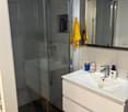 Bathroom with shower cubicle, white cabinet, mirror, sink, faucet, and yellow towel hanging on the wall.