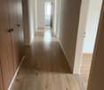 Hallway of the apartment with wooden floors, two doors leading to rooms, one door to the bathroom, a window with a view to the outside.