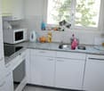 White cabinets, granite countertops, a microwave, an electric kettle, a stove, an oven, a sink, a dishwasher, and a window.