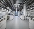Empty laboratory, white countertops, cabinets, monitors, ventilation systems, and illuminated fluorescent lighting