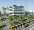 Office building with multiple floors, green facade, large windows, adjacent to a tram track, surrounded by trees and grass