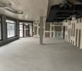 A large empty room with unfinished walls and columns, two doors to the street, windows