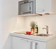 Modern white kitchen with cabinets, induction stove, oven, sink, microwave, plants, and utensils