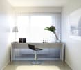 Minimalist modern office with white desk, black swivel chair, desk lamp, window with white curtains, white rug, a framed photograph on the wall.