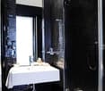 white tiled walls, black tiled floors, white bathtub, white sink, glass shower enclosure