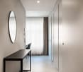hallway with mirror, white walls, wooden flooring, desk and chairs, white curtains