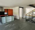 Modern kitchen with black countertops, glass cabinets, and red cabinets. Stainless steel stove and oven. Open space with staircase.