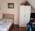 Bedroom with wooden bed, wardrobe, wooden floor, wall painting, and various items on a shelf