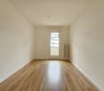 Empty room with white walls, hardwood flooring, and a radiator. The room has a window that provides natural light.