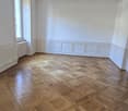 Spacious room with white walls, wooden parquet flooring in a herringbone pattern, and a single light fixture on the ceiling.