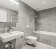 Large bathroom with grey tile walls, white sink, toilet, and bathtub with shower head