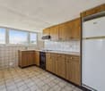 Spacious kitchen with wooden cabinets, tiled floor, oven, refrigerator, and large windows providing natural light