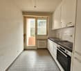 The image shows a small kitchen with a window, tile flooring, white cabinets, and a stove/oven unit. The kitchen appears to be in a residential setting with a view of the outdoors through the window.
