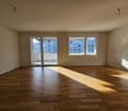 Spacious living room with hardwood flooring, large windows, and a balcony or terrace providing natural light and a view of the surrounding buildings.