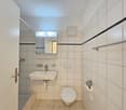 small bathroom with shower, toilet, sink, mirror, white tiled walls, white tiled floor
