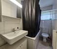 Bathroom: sink, bathtub, toilet, white tile, mirror, shower curtain, radiator, cabinet