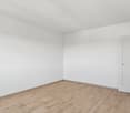 an empty room with white walls, white ceiling, wooden floor, and white door