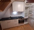 kitchenette, white cabinets, black countertops, stove, sink, open refrigerator