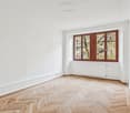An empty room with wooden herringbone flooring, white walls, and a window with wooden frame