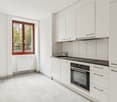 Kitchen with white cabinets, black countertops, white tile flooring, modern white oven and sink with a faucet, and a window with view outside.
