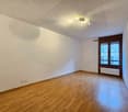 Empty room with wooden floor, white walls, radiator, large window, and a ceiling light