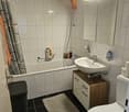 Bathroom: bathtub, toilet, sink, shower, tiled walls, cabinet with drawers, towels, shower curtain, mirror with shelf