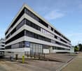modern office building, multiple windows, concrete exterior, multiple floors, parking area in front