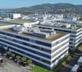 Multi-story office building with large windows, parking spaces, green roofs, green spaces