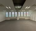 large empty room, white walls, large windows with white shutters, gray carpet, white ceiling with lights, two white radiators.