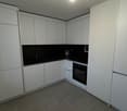 Modern kitchen with white cabinetry, black countertops, dishwasher, washing machine, and built-in oven and microwave