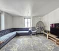 modern living room with L-shaped sofa, wooden side table, TV, armchair, hanging basket chair, potted plant, carpet, two windows