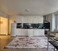 White kitchen with tile floor, microwave, refrigerator, countertop, sink, stove, cabinets, rug, and dining area with a table and chairs.