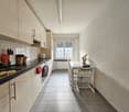 white kitchen, white cabinets, black countertops, stainless steel sink, dishwasher, washing machine, tile floor, dining table with 4 chairs, gas stove, window