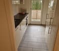 modern kitchen, tile flooring, wooden counter, white cabinets, modern sink, black stove, glass door