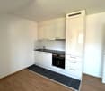 modern kitchen with white cabinets, black countertops, built-in oven, sink, faucet, wooden floor, white walls