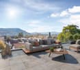 Spacious outdoor terrace with comfortable gray sofa, wooden coffee table, and decorative elements. The terrace offers a scenic view of the city and surrounding hills.